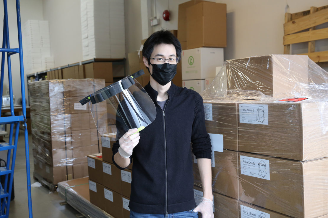 One of Tinkerine's employees shows a face shield for the deaf, in front of more boxes of face shields