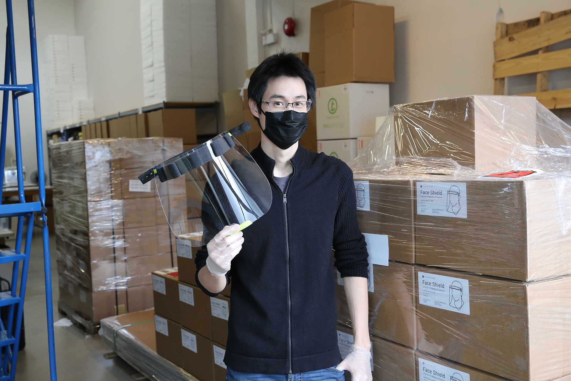 A tinkerine employee shows off a face shield, in front of boxes of face shields for the deaf and hard of hearing