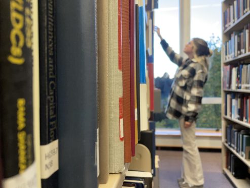 Person browsing a bookcase, photo by Karley Sider.