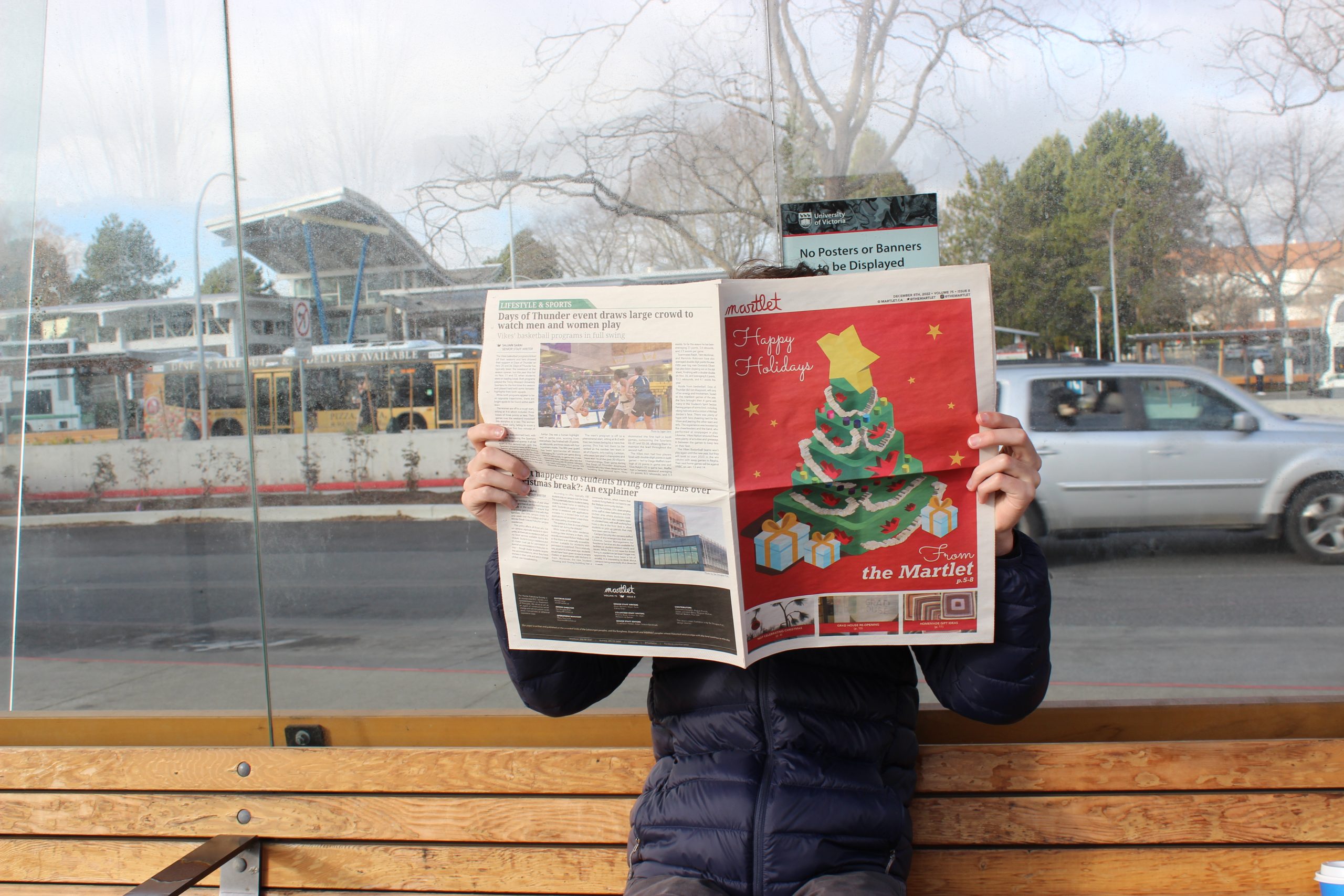 Someone at a bus stop reading the Martlet's 2023 holiday issue, photo by Mary MacLeod.