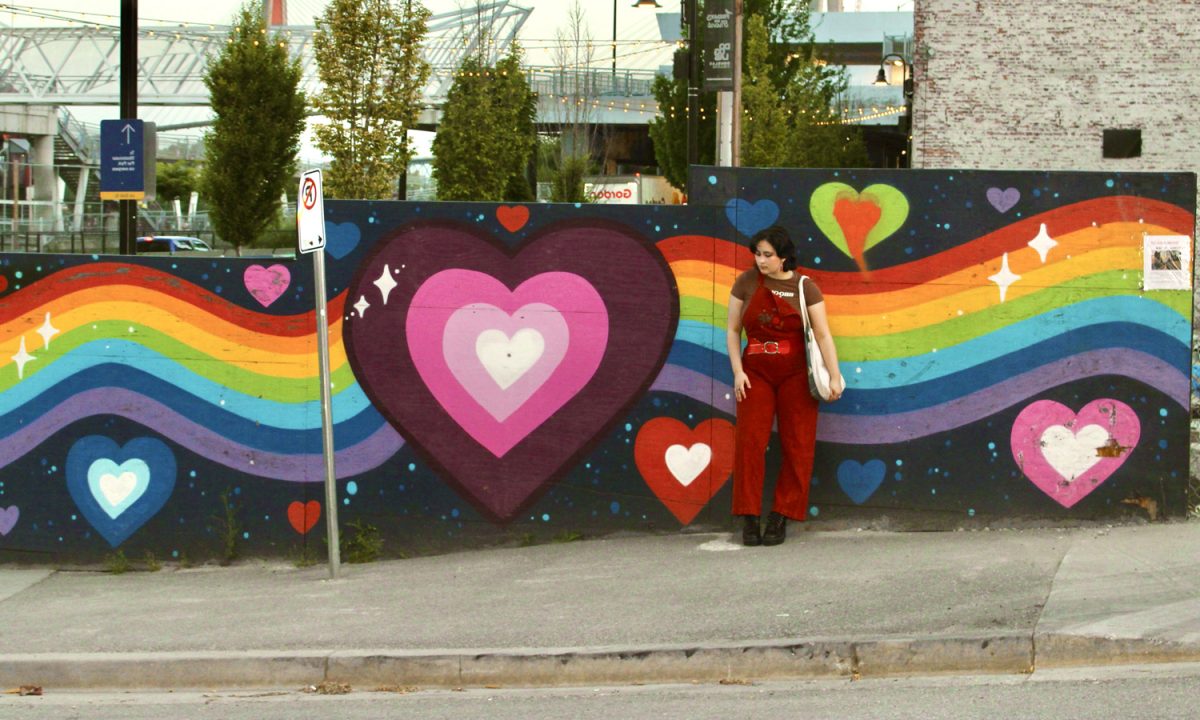 A rainbow pride mural with someone standing in front of it. Photo by Cooper Anderson.