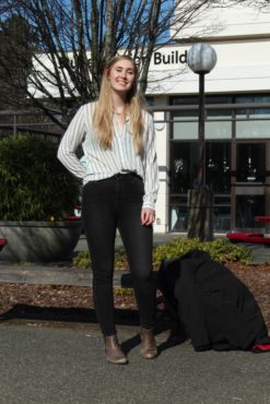 Ainsley Kerr, Candidate for Campaigns and Community Relations with Envision UVic, stands in front of the SUB wearing a striped top and black jeans.