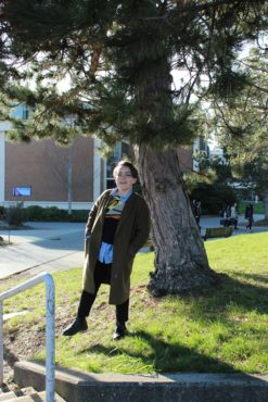 Ciel Arbour-Boehme, candidate for Director of Campaign and Community Relations with the Purple Party wears a long green quote, collared top, and dark pants on campus. 